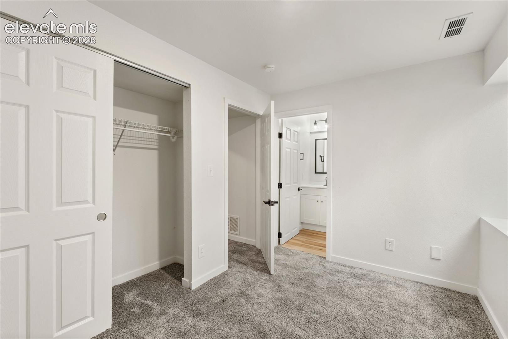 Interior room featuring wall-to-wall carpeting, a walk-in closet with built-in shelving, and a six-panel interior door