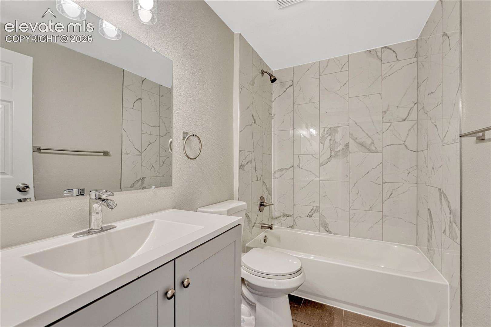 Integrated bathtub with tiled surround, light-toned vanity with undermount sink, and chrome fixtures