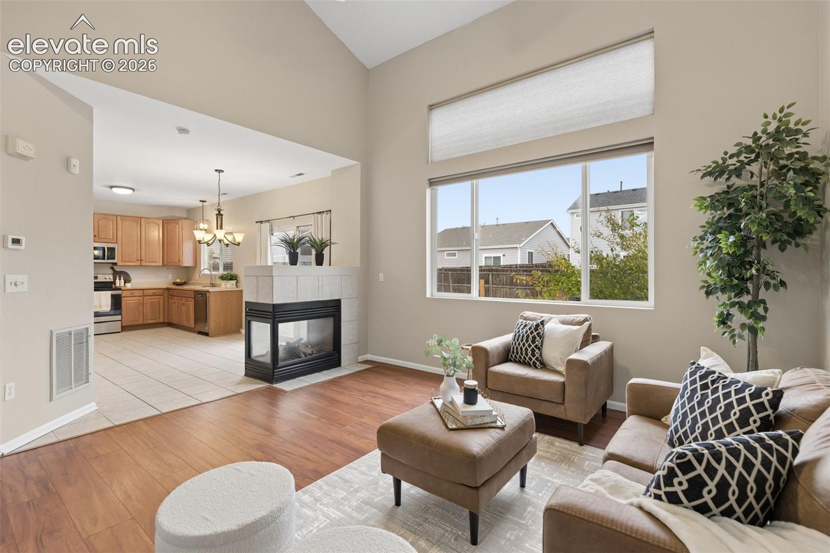 Vaulted ceilings, corner fireplace with tile surround, wood-finish flooring, and large windows with horizontal blinds