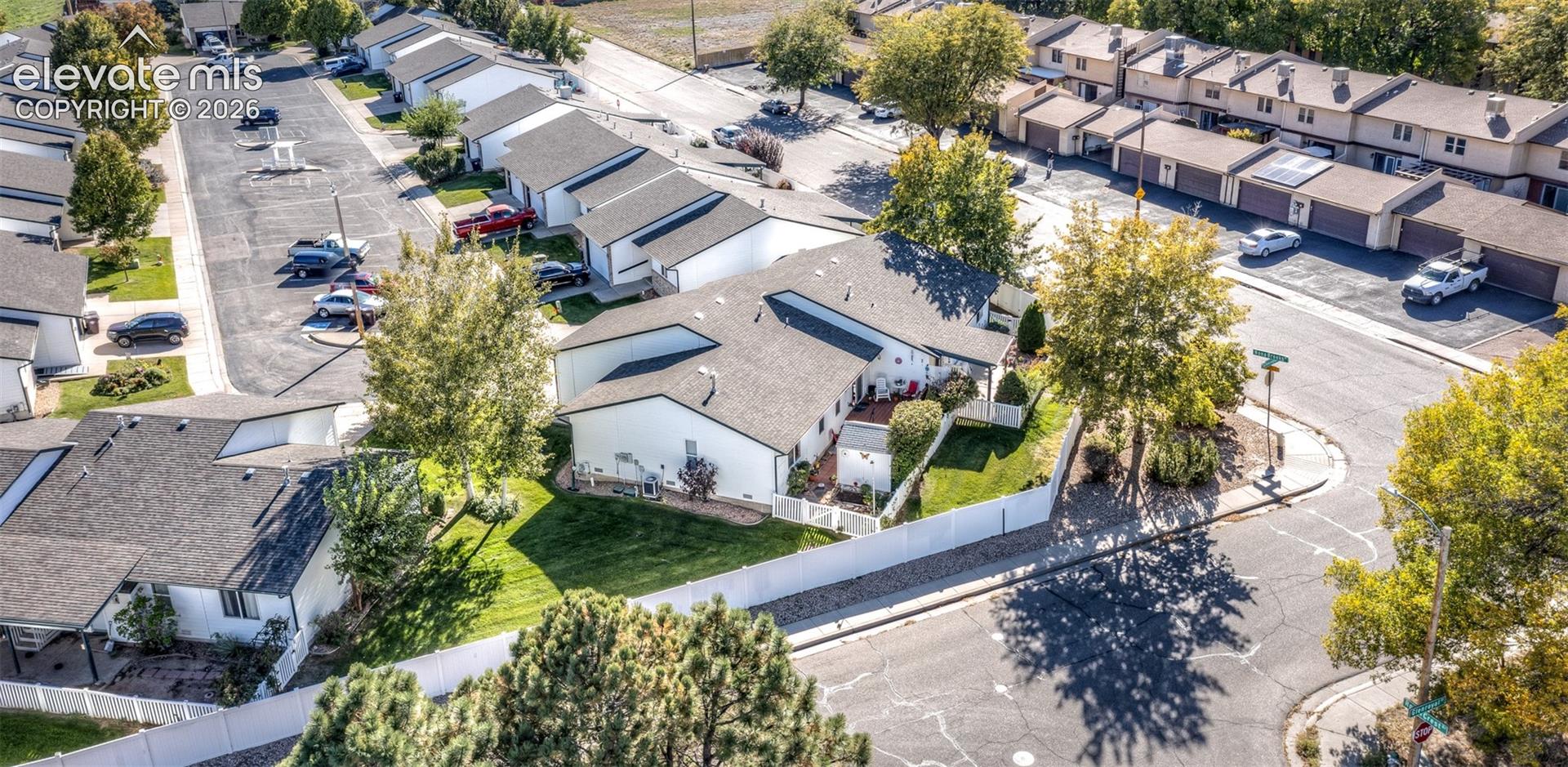 Aerial view featuring a multi-unit property with composite shingle roofing, white exterior siding, paved surface parking, and perimeter privacy fencing