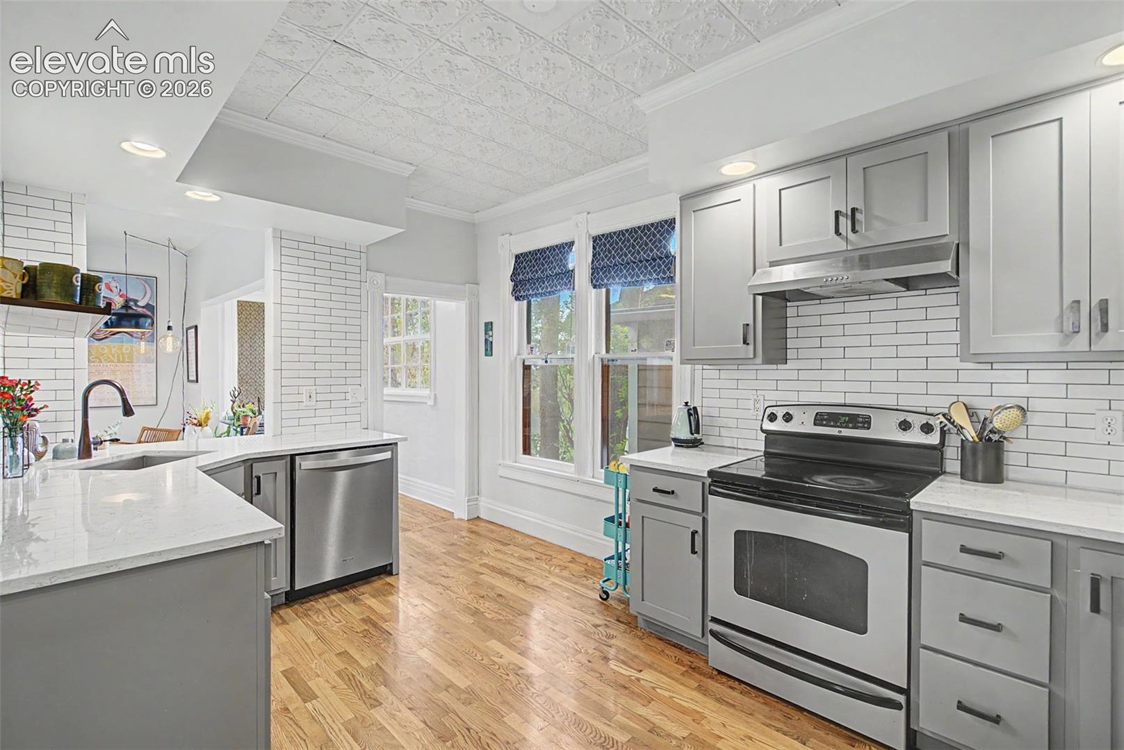 Updated kitchen with light gray cabinetry, Victorian-style ceiling tile, white tile backsplash, white stone countertops, and hardwood flooring.