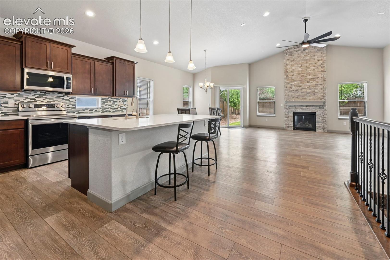 Kitchen featuring dark wood cabinetry, a quartz-topped island, stainless steel appliances, wood-finish flooring, and a floor-to-ceiling stone fireplace