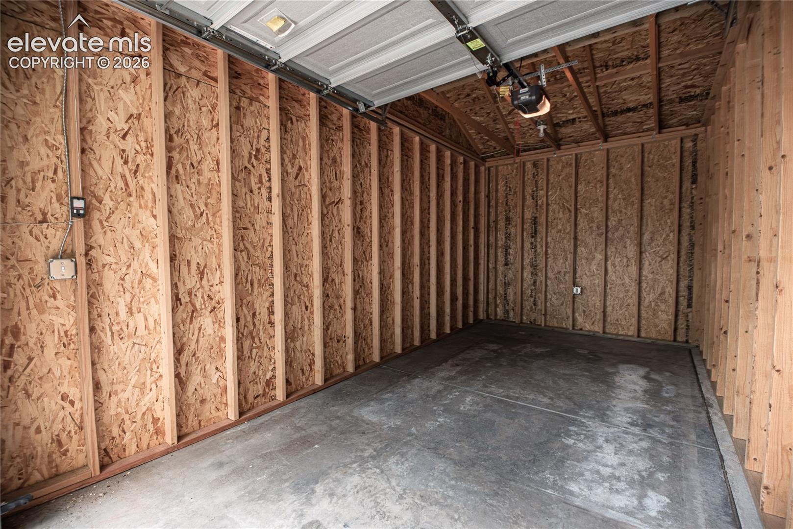 Single-bay garage featuring a concrete floor, exposed wooden stud walls with oriented strand board, and an automatic garage door opener