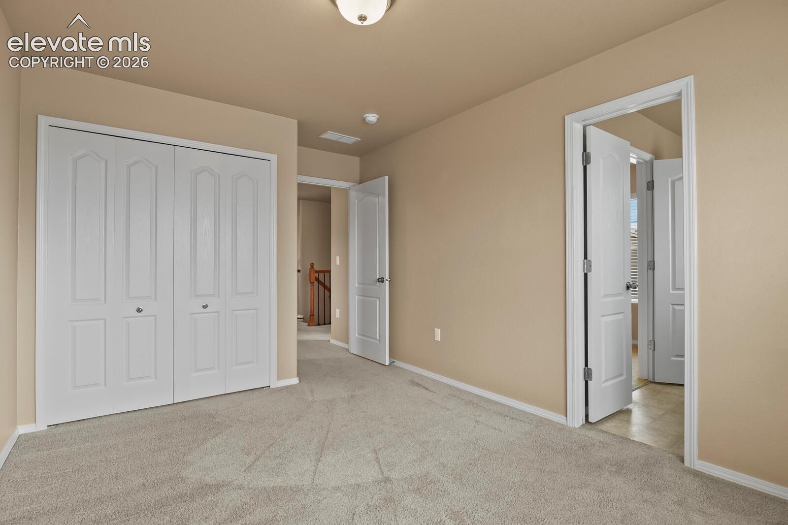 Neutral tone wall paint, light gray carpet flooring, white bi-fold closet doors, white paneled interior doors, and a ceiling-mounted light fixture
