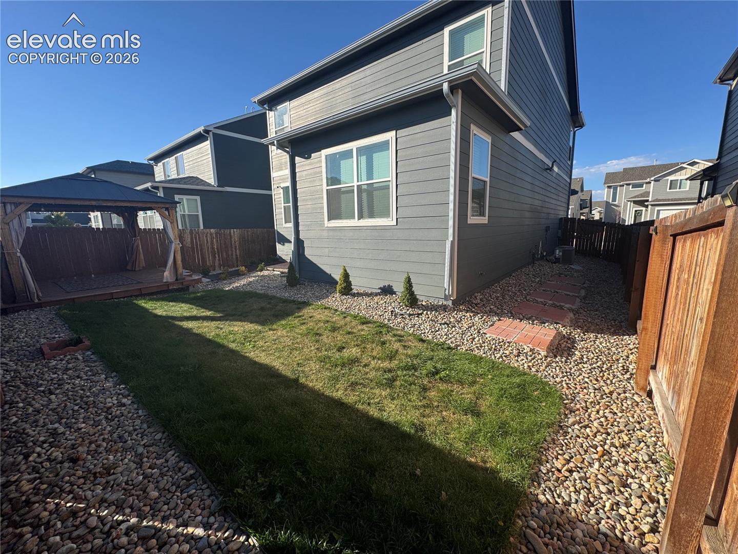 Fenced backyard featuring horizontal siding, a central grass lawn, gravel hardscaping, stone pavers, and a built-in wooden structure