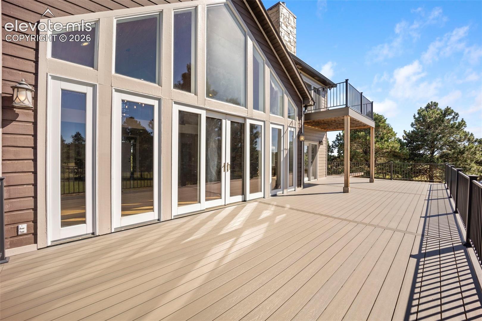 Expansive outdoor deck featuring composite decking, black metal railings, and a direct entrance to the interior through multiple glass doors