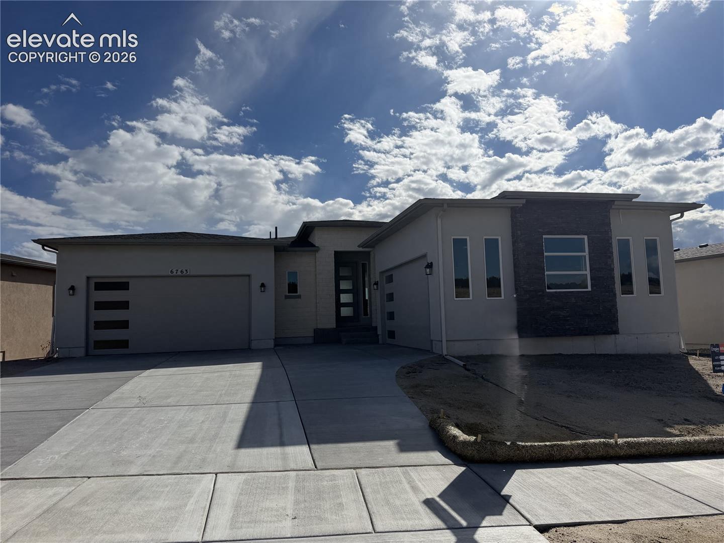 Modern exterior featuring a smooth stucco facade, stacked stone masonry accents, a three-car garage with horizontal glass paneling, and a contemporary entry door with glass inserts