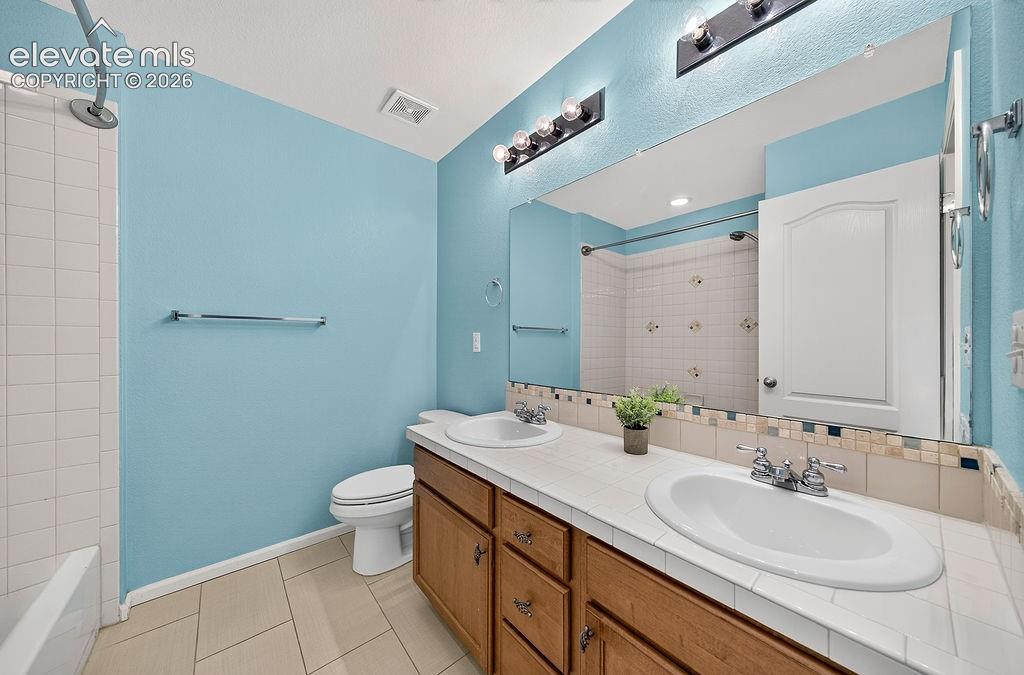 Dual vanity with integrated sinks, wood-finish cabinetry, tile countertop, and a large wall mirror