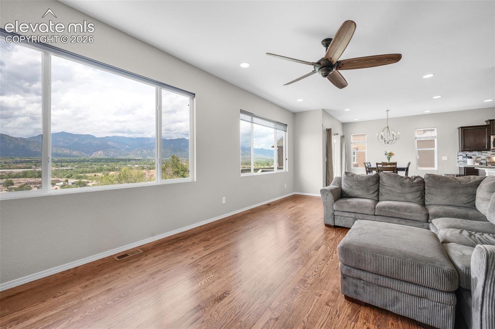 Open concept living area featuring expansive windows with a dramatic front range view, wood-finish flooring, recessed lighting, and a ceiling fan
