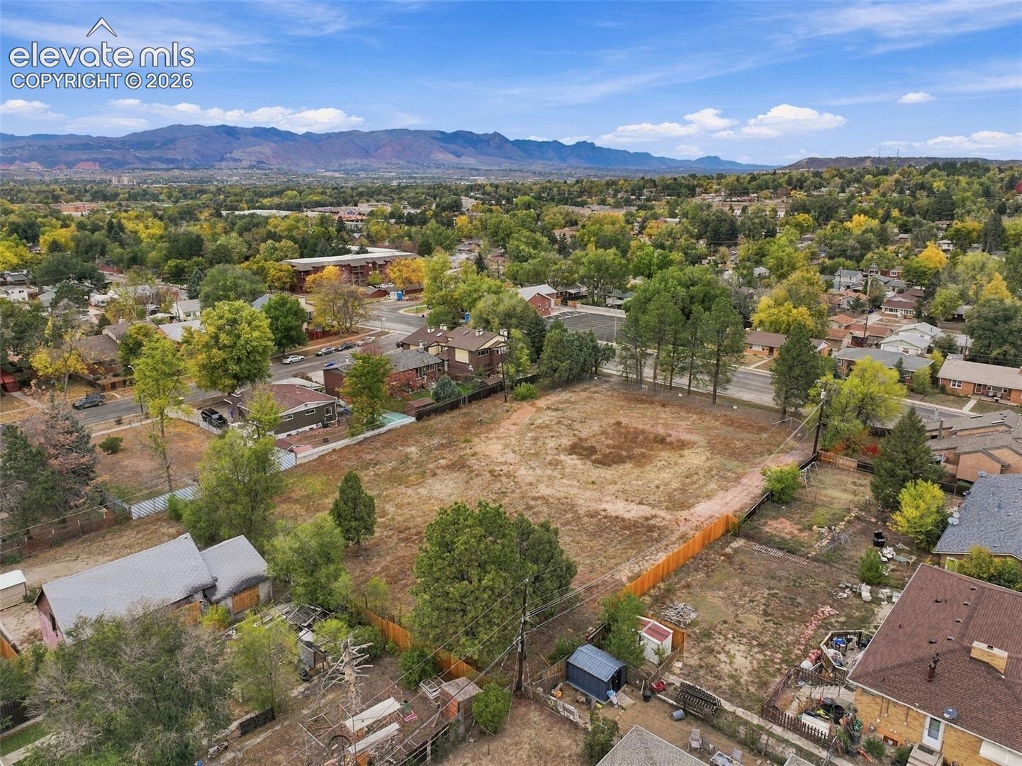 Expansive undeveloped lot featuring partial wood fencing, mature trees, and a mountain range backdrop