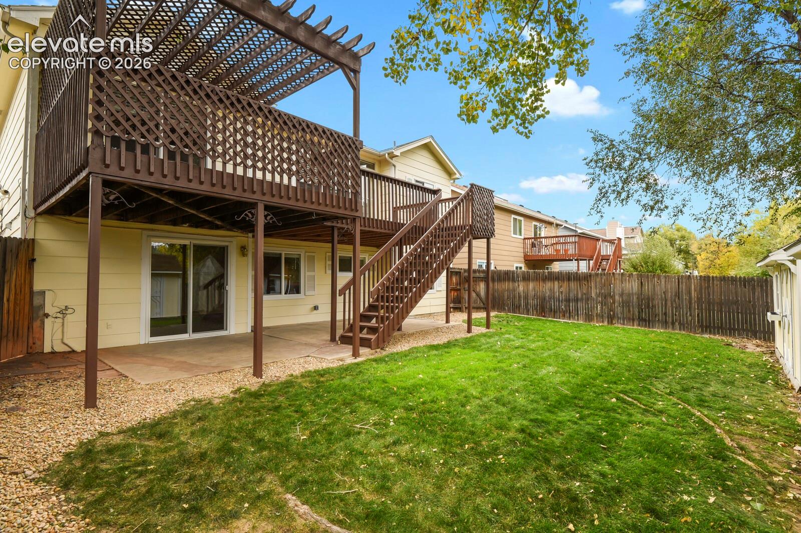 Rear exterior featuring an elevated wood deck with a pergola, staircase access, concrete patio, and fenced backyard
