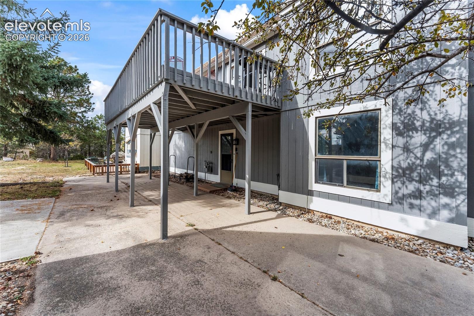 Exterior featuring vertical siding, elevated wooden deck, concrete patio, and large glass windows