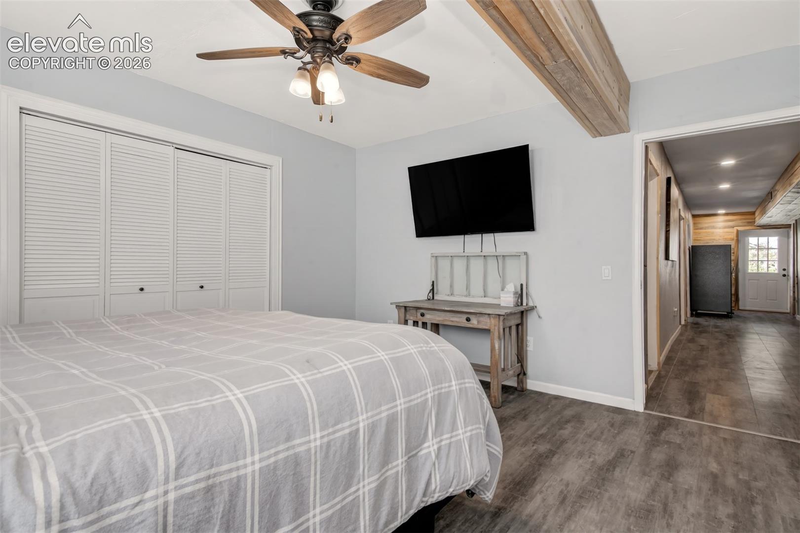 Room featuring wood-finish flooring, a ceiling fan with integrated lighting, bifold closet doors, and an exposed ceiling beam