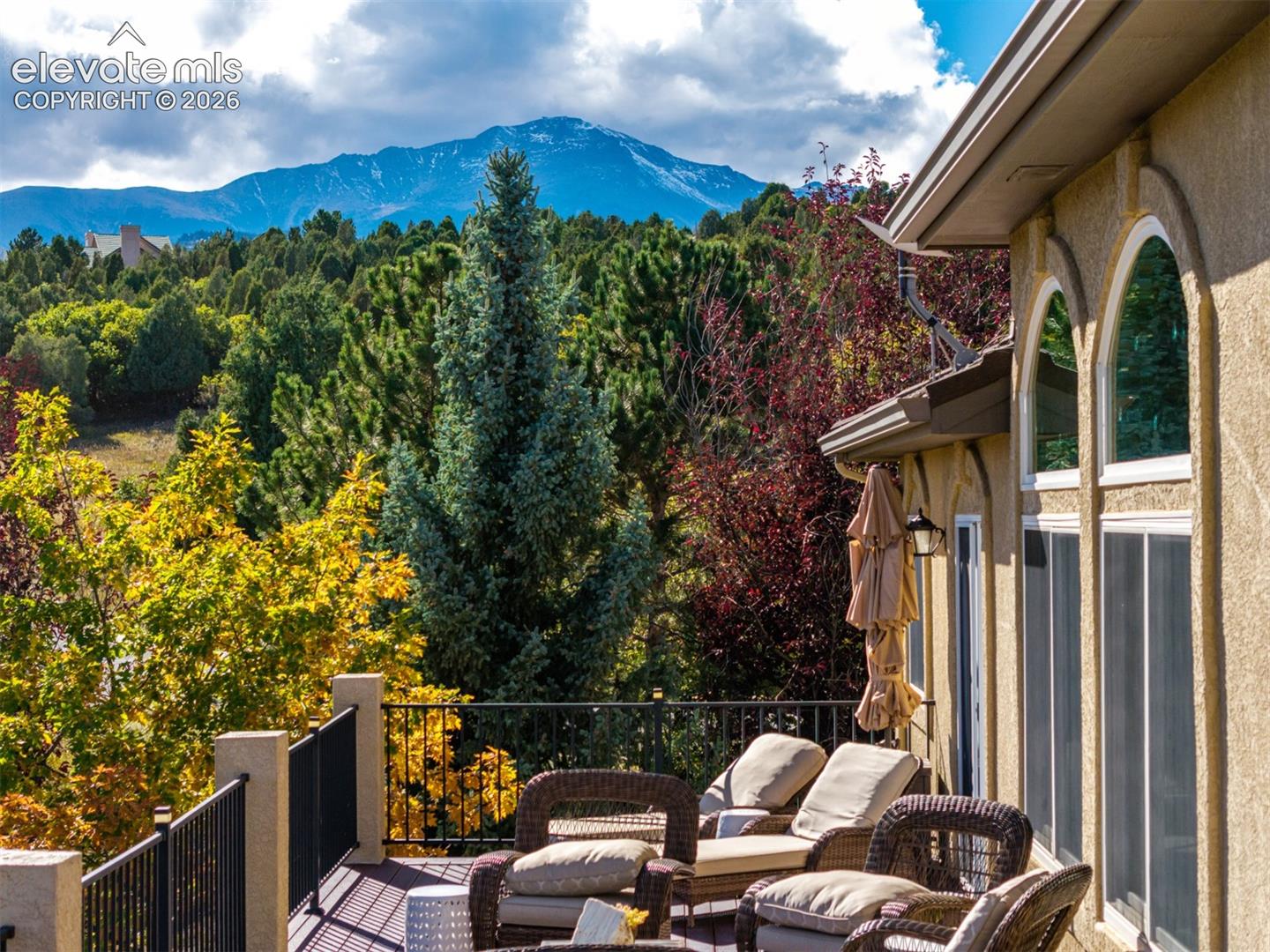 Spectacular views of Pikes Peak from the side of the home and back balcony, showcasing the mountain's distinctive summit and rugged ridgelines rising above the surrounding foothills. Mature evergreens and vibrant autumn foliage frame this iconic Colorado landmark, creating a beautiful mountain backdrop for the property in the gated Juniper Ridge at Cedar Heights community.