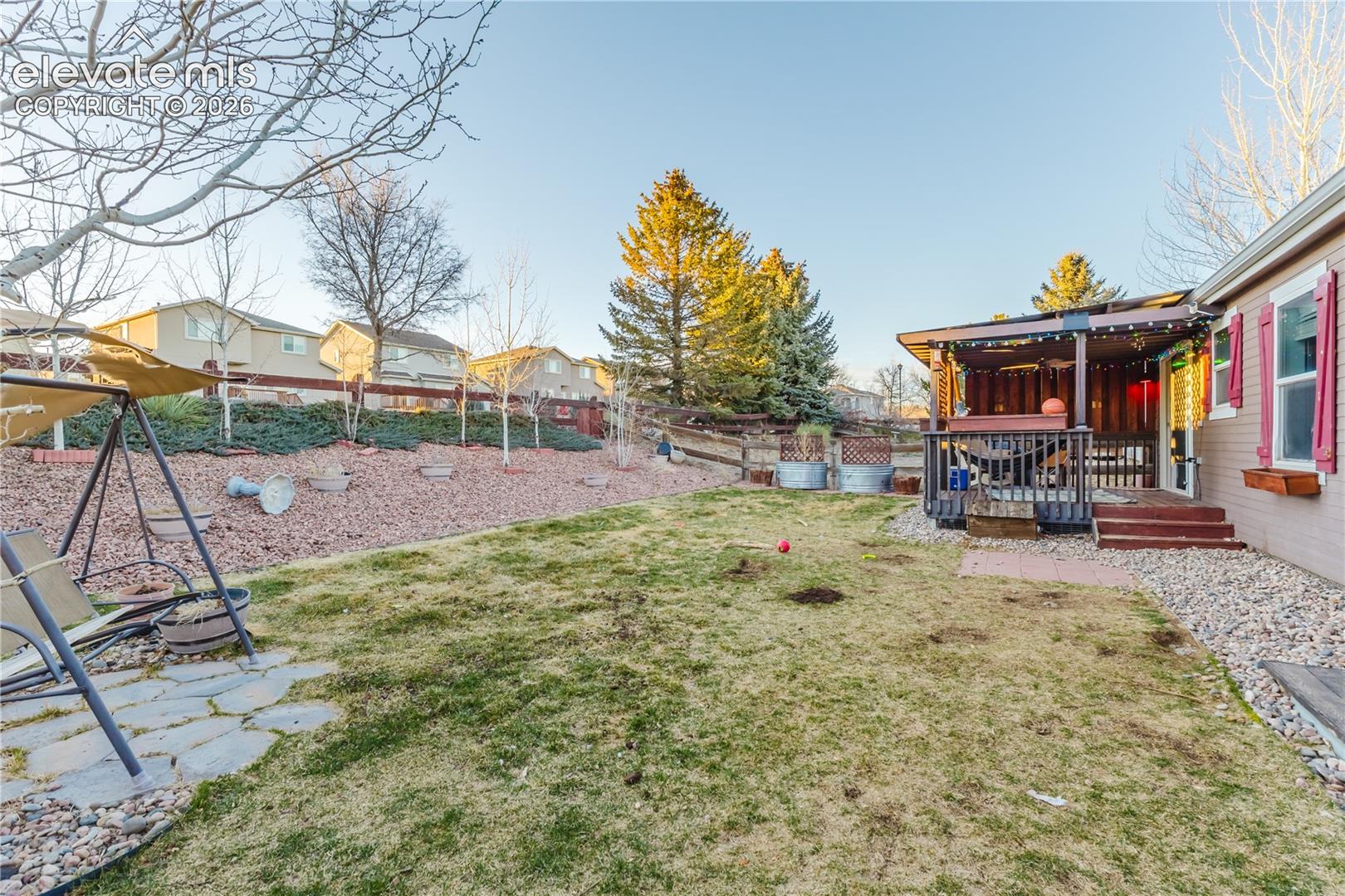 Expansive backyard featuring a covered patio, tiered landscaping with mature trees, and a stone patio area