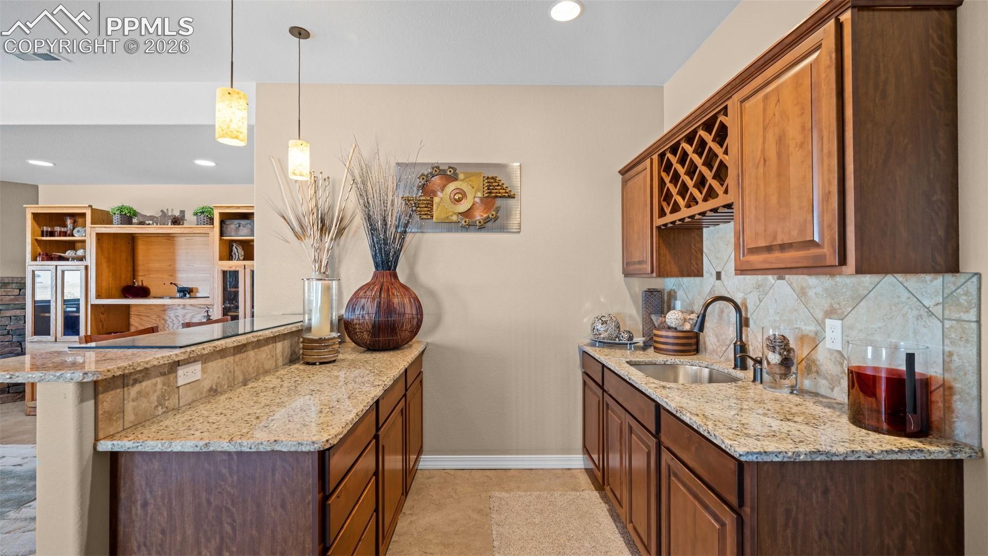 Gorgeous wet bar with a peninsula, light stone counters, backsplash, decorative light fixtures