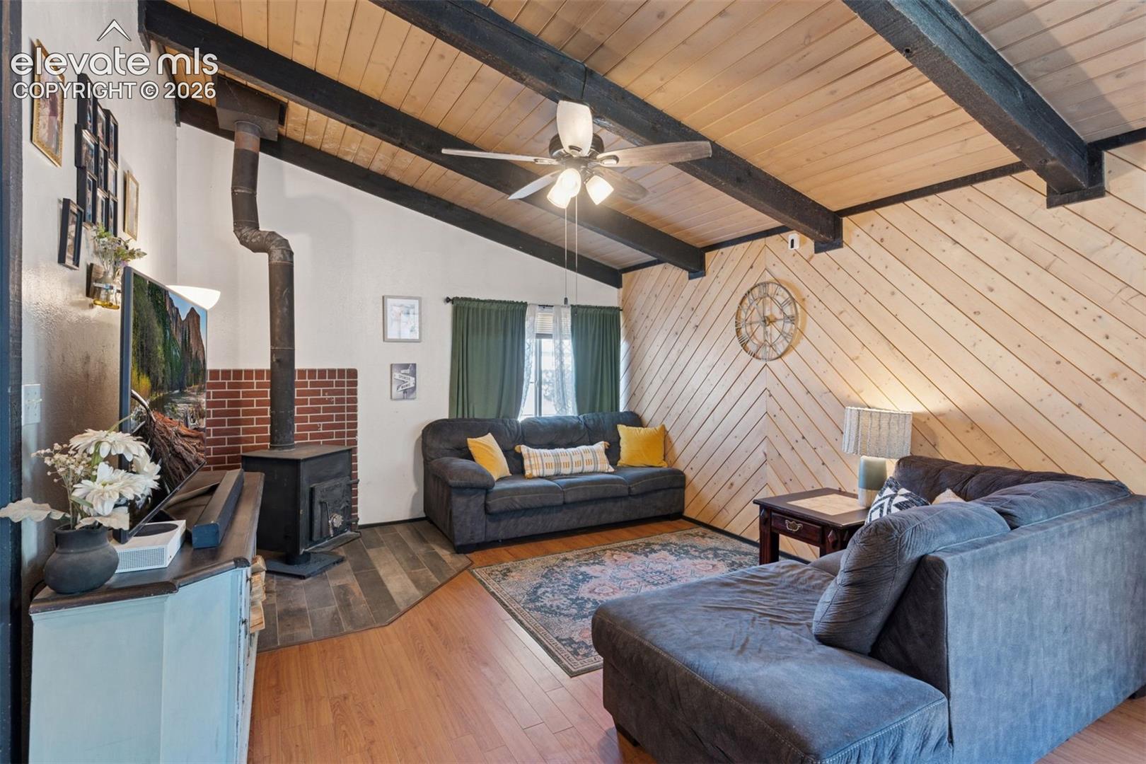 Inviting living room featuring a warm wood-paneled vaulted ceiling, exposed beams, and a cozy wood-burning stove—creating a comfortable, cabin-style atmosphere ideal for year-round use or rental appeal
