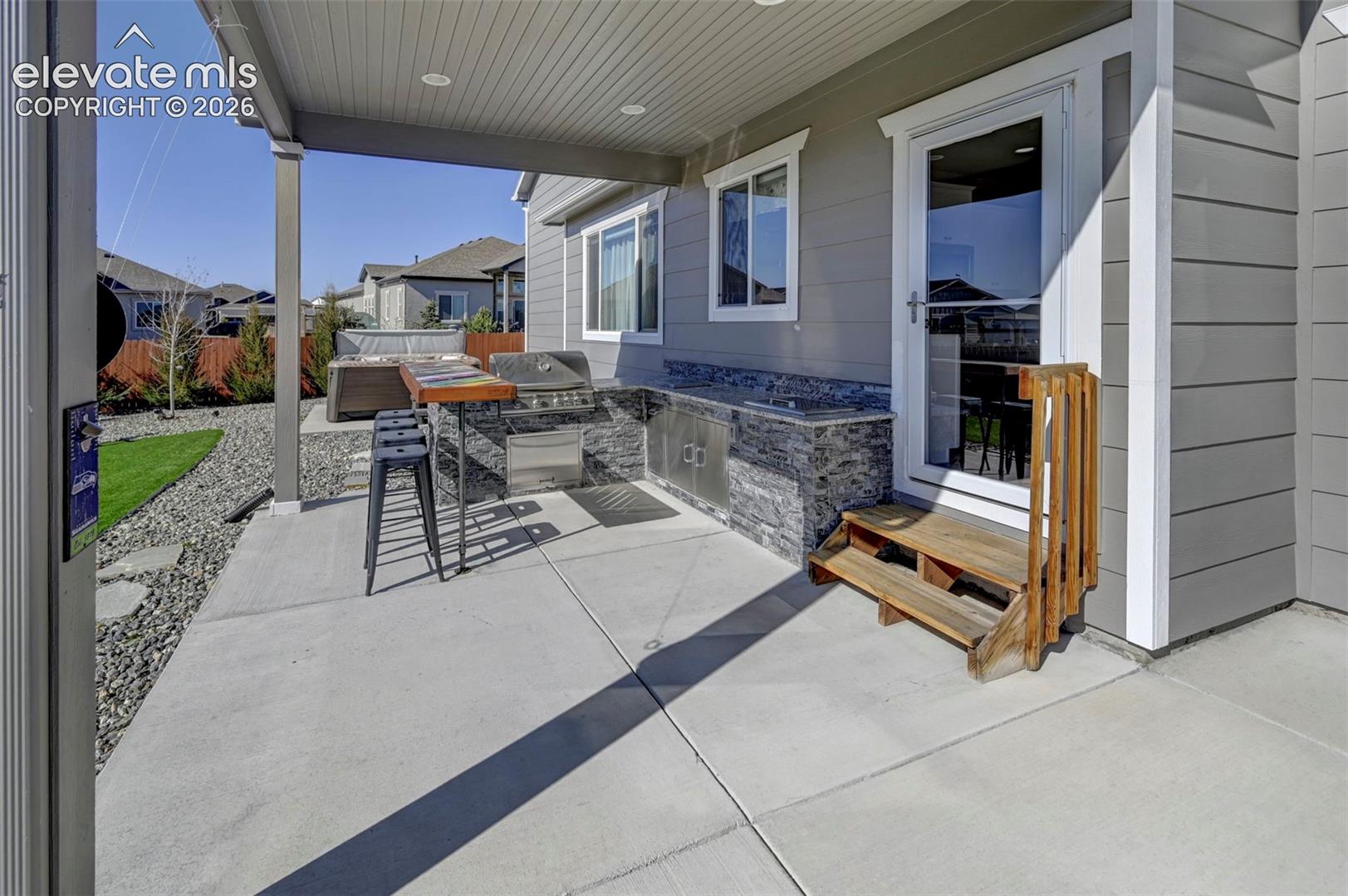 Covered concrete patio with built-in outdoor kitchen, integrated grill, and stone-finish cabinetry