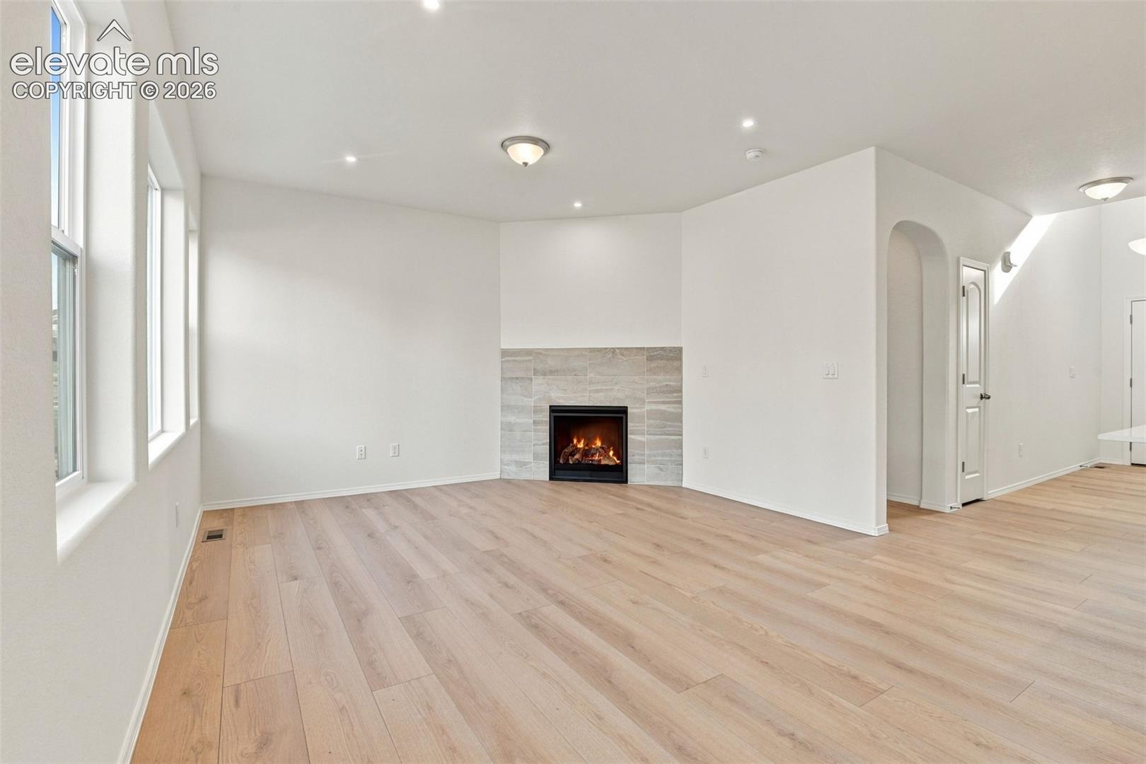Neutral-toned space featuring wood-finish flooring, a fireplace with a textured tile surround, recessed lighting, arched entryway, and multiple paneled windows