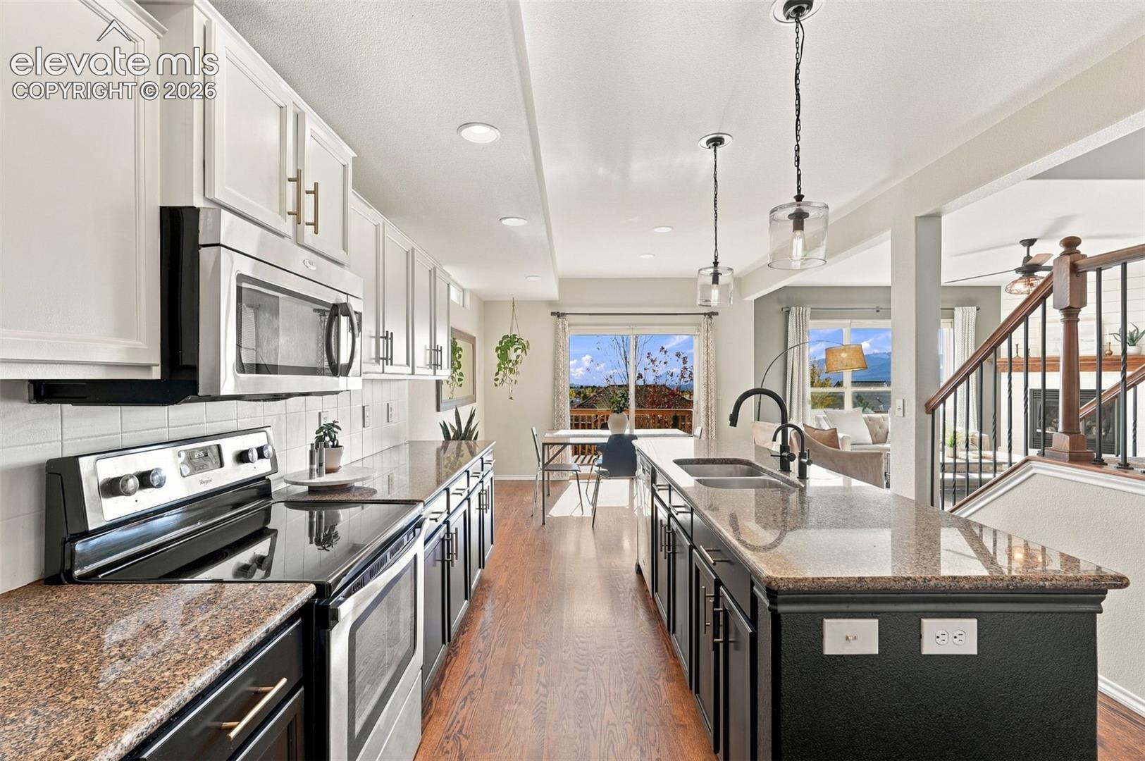 Kitchen featuring white and black cabinetry, stone-finish countertops, stainless steel appliances, wood-finish flooring, and pendant lighting