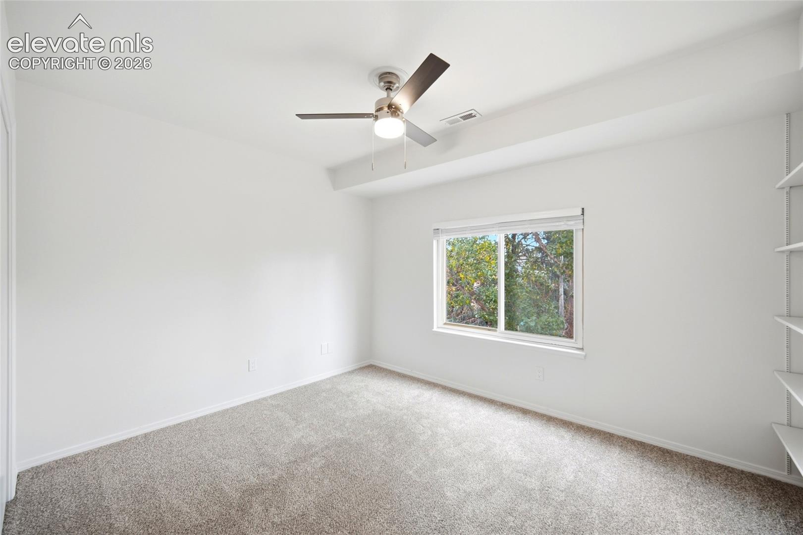 Neutral wall finishes, plush carpeting, ceiling fan with integrated lighting, slider window, and built-in white shelving