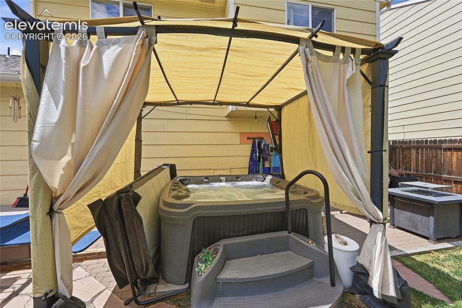 Outdoor spa featuring a molded basin, integrated entry steps, metal frame gazebo, and stone paver patio