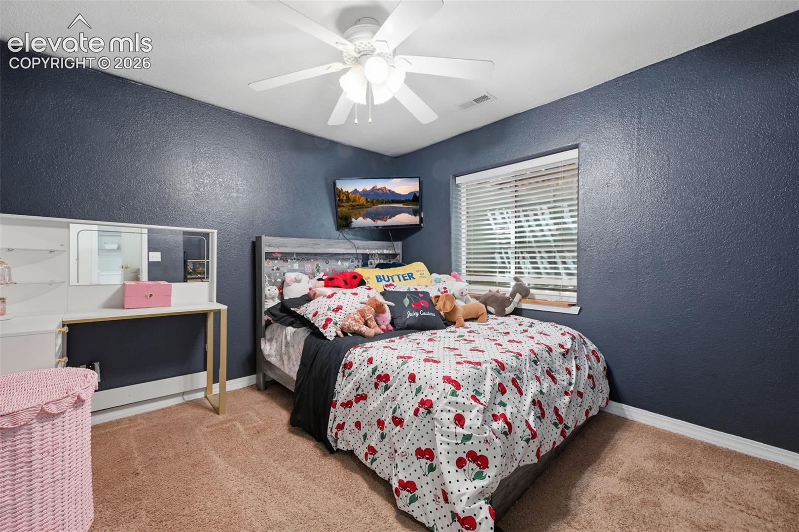 Textured walls, recessed window with blinds, ceiling fan, carpet flooring, and built-in desk
