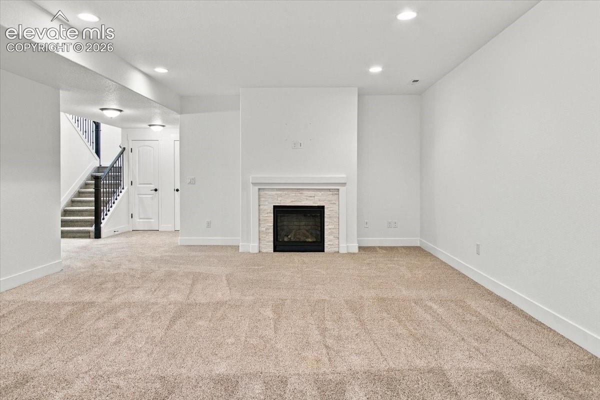 Fireplace with a stacked-stone surround, recessed lighting, and wall-to-wall carpeting
