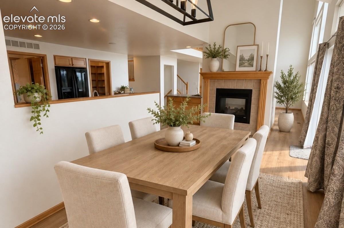 Dining area featuring a fireplace with a wood mantle and tile surround, recessed lighting, and wood-finish flooring, virtual staging