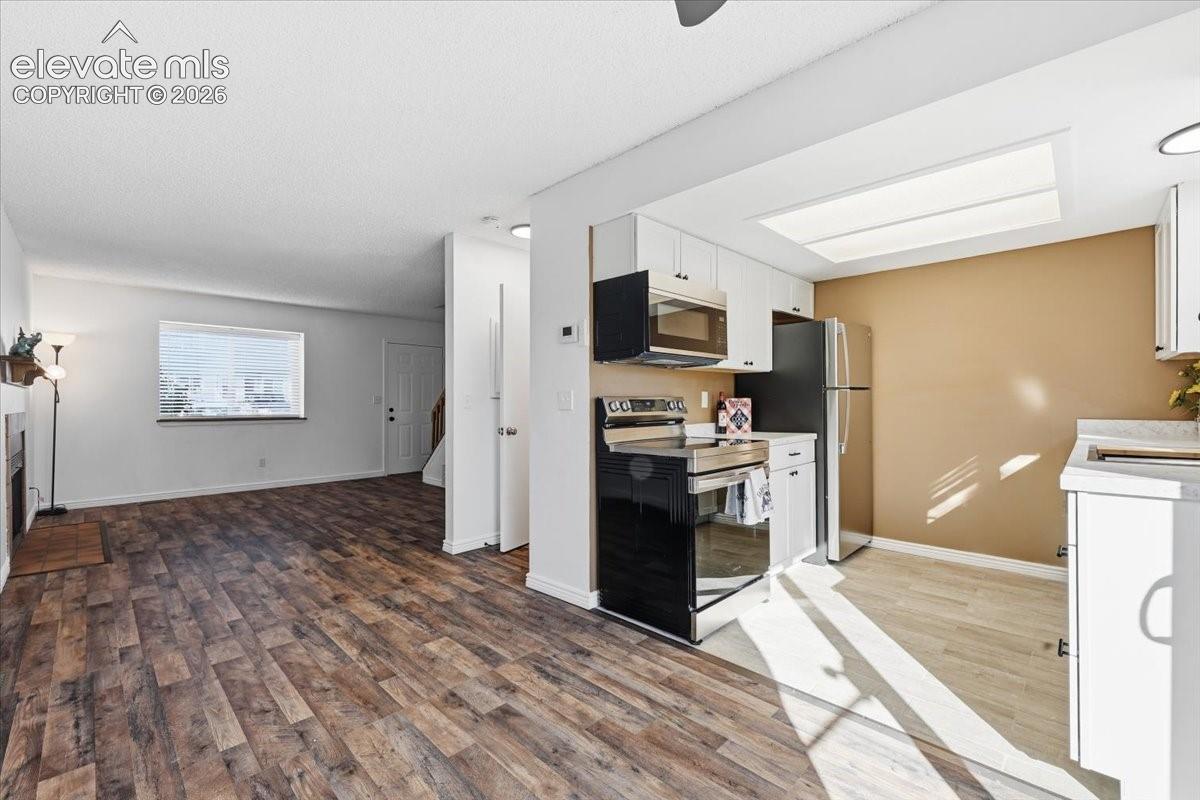 Wood-finish flooring throughout, kitchen with white cabinetry, stainless steel appliances, and a built-in microwave