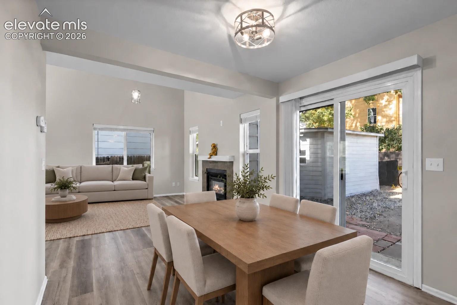 Open-concept interior featuring wood-finish flooring, a fireplace with a stone-tile surround, sliding glass patio doors, and a multi-light drum pendant fixture