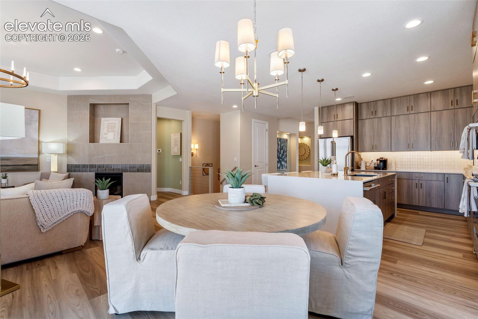 Kitchen featuring flat-panel cabinetry, a quartz-topped center island with integrated sink, wood-finish flooring, recessed lighting, and a stone-clad fireplace with recessed niche