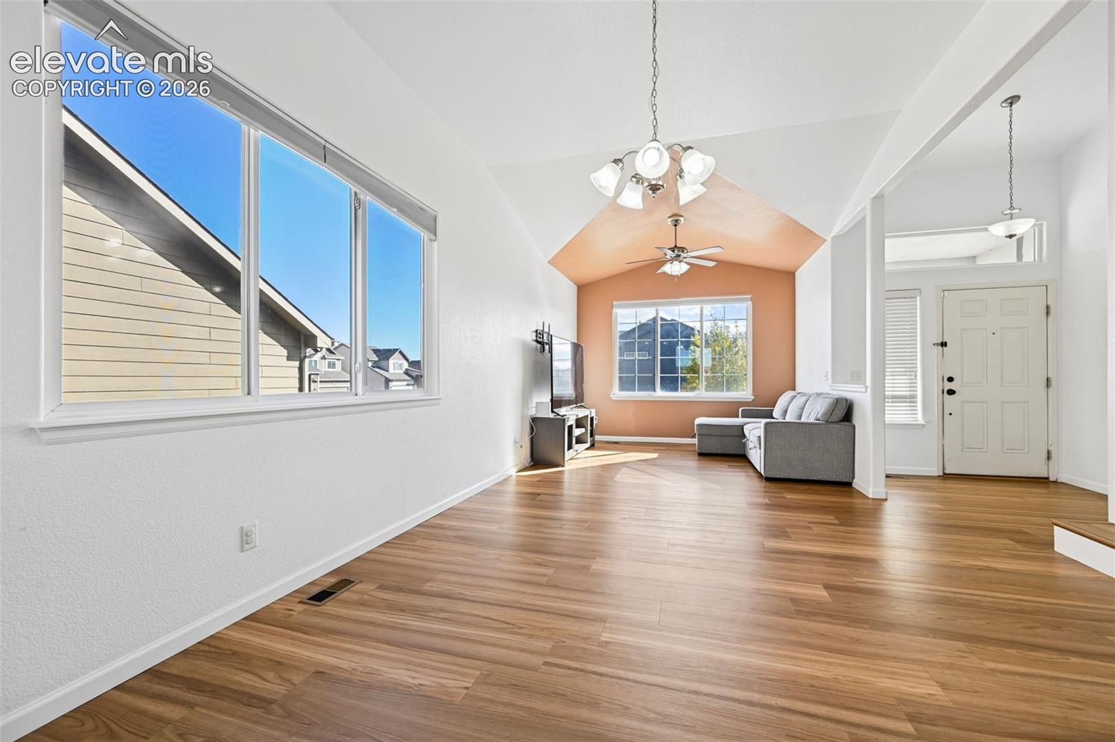 Vaulted ceiling with a five-light chandelier, wood-finish flooring, and expansive windows