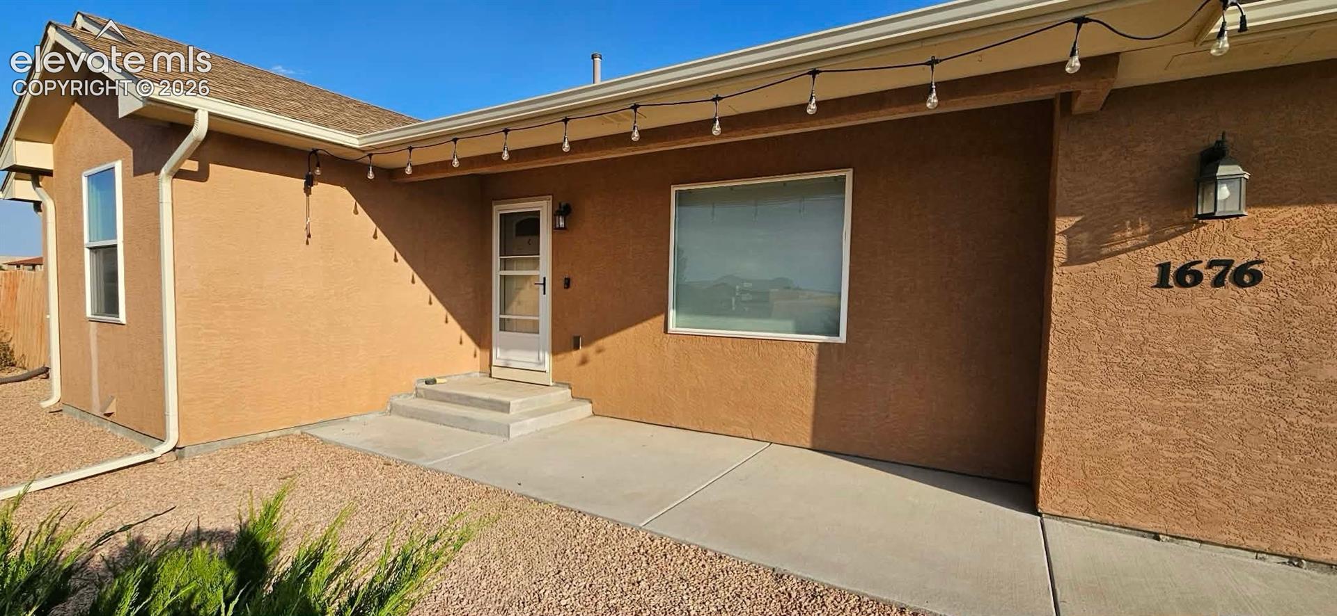 Stucco exterior with a covered concrete entry, front door featuring a storm door, and xeriscaped landscaping