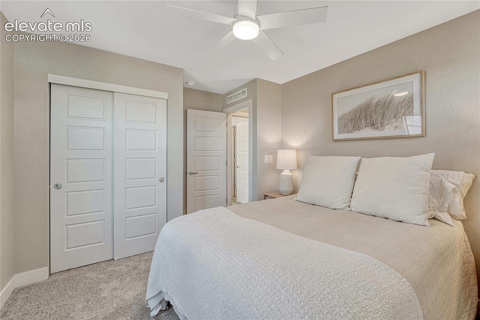 Room featuring neutral wall tones, white four-panel interior doors, a sliding-door closet, wall-to-wall carpeting, and a central ceiling fan with an integrated light fixture