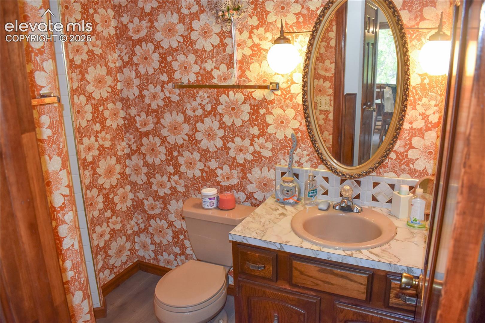 Vanity with an oval mirror, dual wall-mounted light fixtures, and a cultured marble countertop featuring an integrated sink