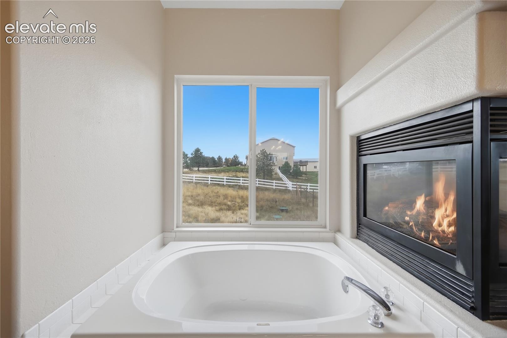 Oval soaking tub with a white surround, integrated three-sided fireplace, and large sliding window