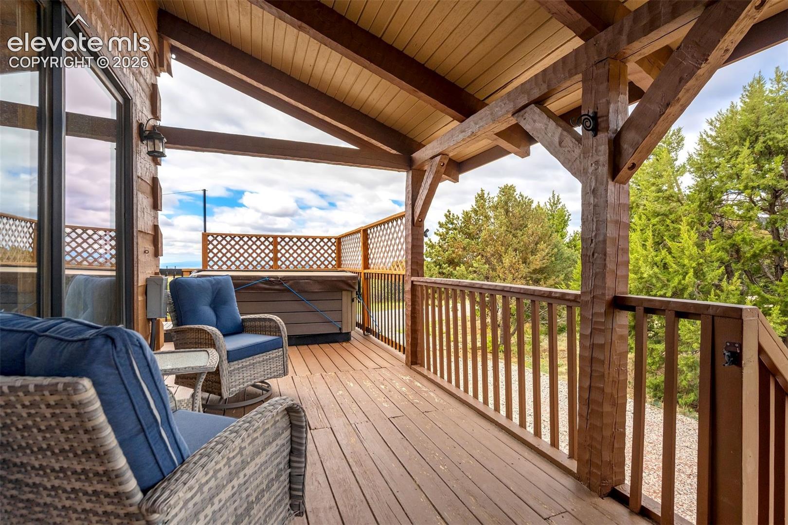 Covered deck featuring a built-in hot tub, durable wood-finish flooring, and exposed timber beams