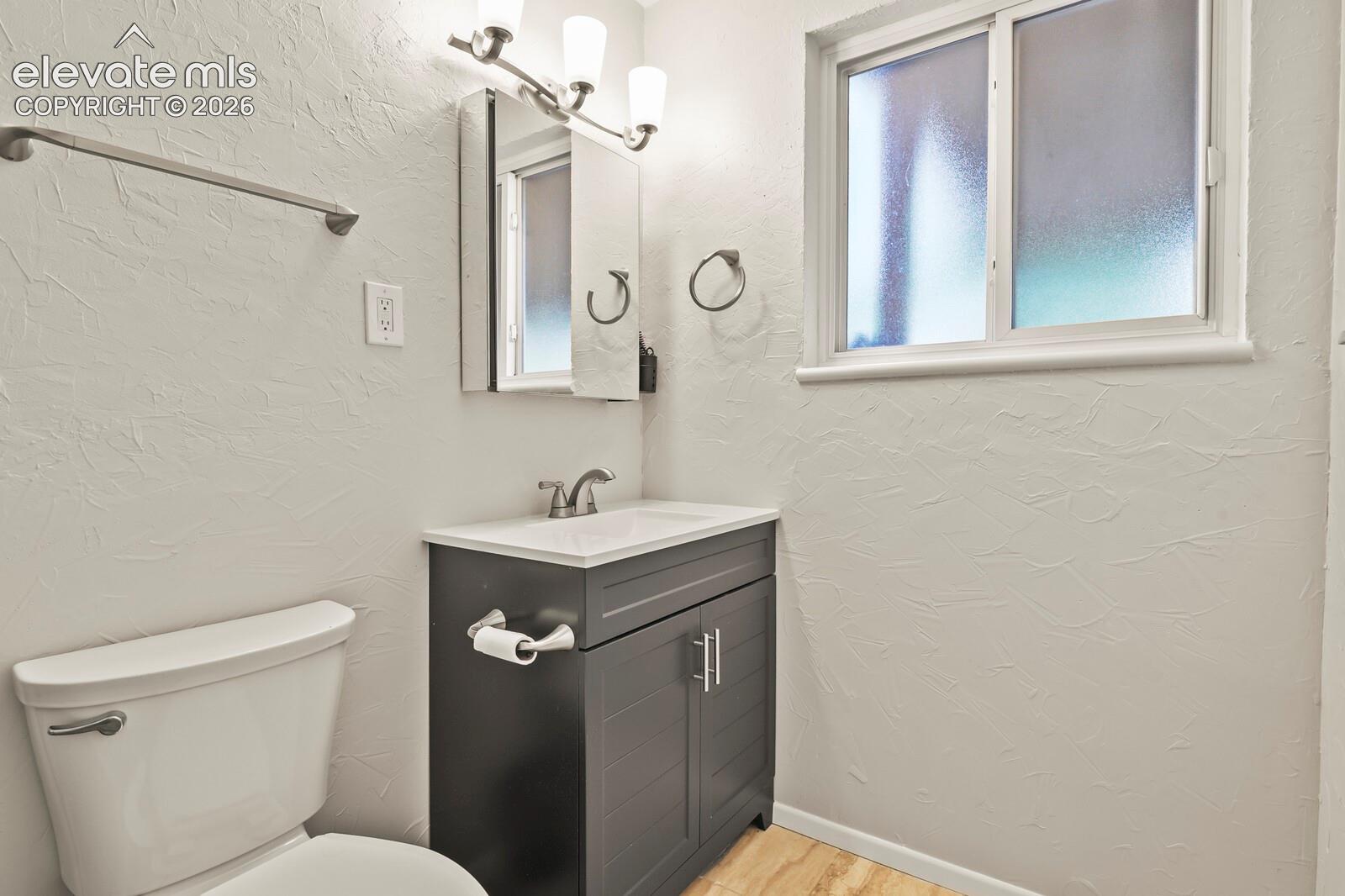 Bathroom featuring a gray vanity with an integrated sink, brushed nickel faucet, and overhead three-light fixture