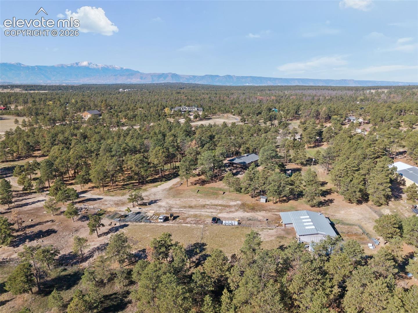 Aerial perspective of expansive wooded acreage featuring a detached metal-roofed structure and mountain backdrop