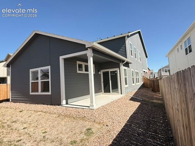 Exterior featuring dark gray siding, white trim, covered patio, sliding glass door, and gravel landscaping