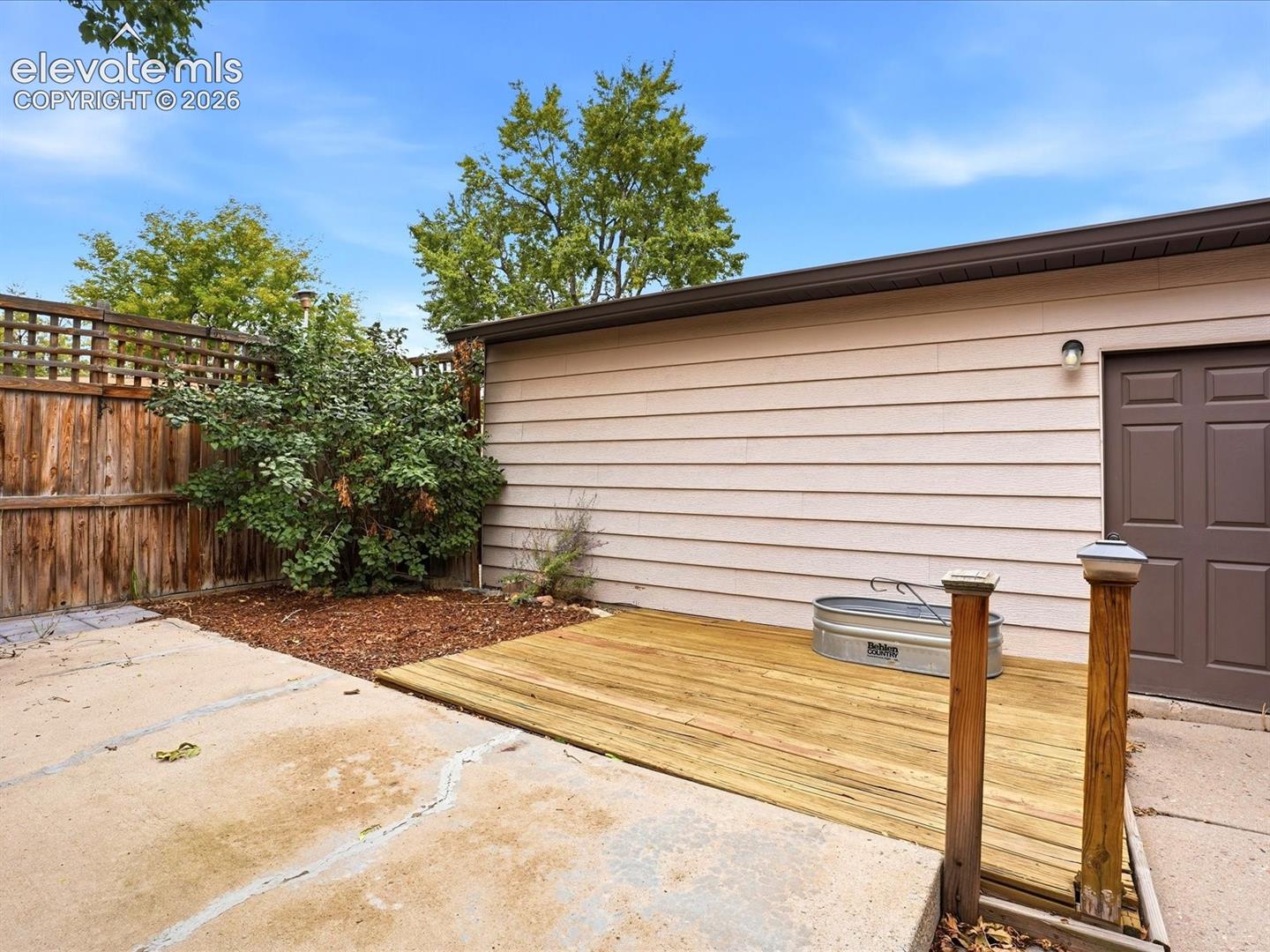 Exterior space featuring a wood deck, horizontal lap siding, a solid-panel door, and wood-slat perimeter fencing