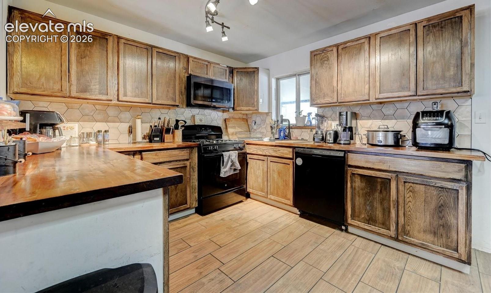 Kitchen featuring wood cabinetry, butcher block countertops, hexagon tile backsplash, black appliances, and wood-finish tile flooring