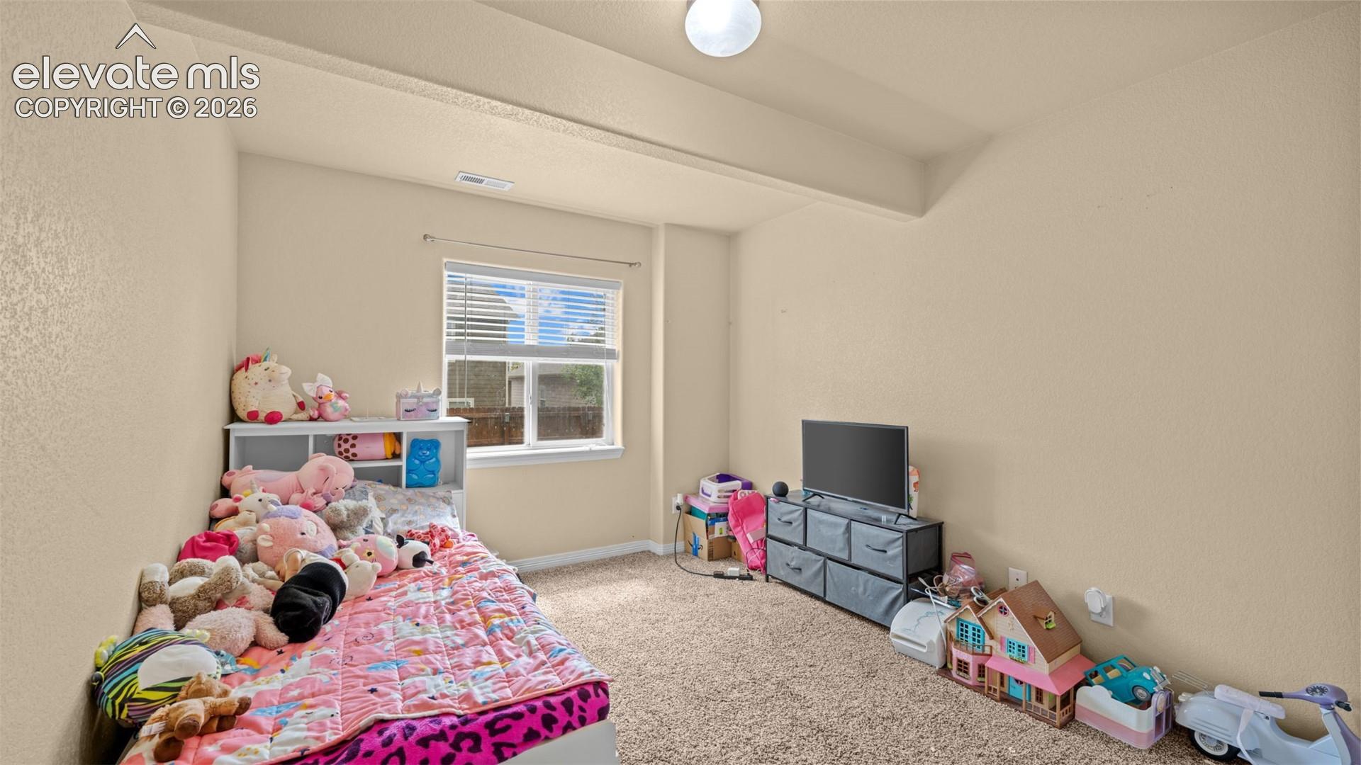 Carpeted room with a single window featuring blinds, textured walls, and a ceiling light fixture