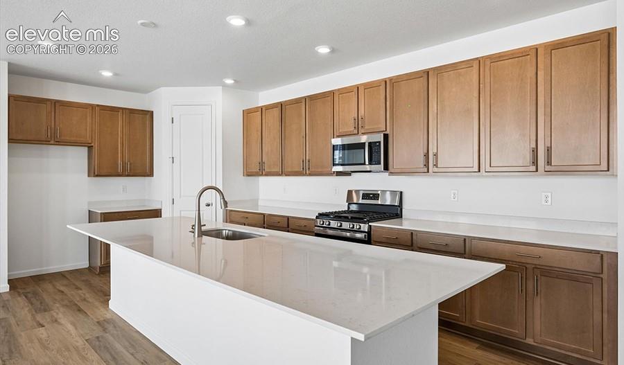 Kitchen featuring wood-finish cabinetry, stone-surface countertops, a center island with an undermount sink, recessed lighting, and stainless steel appliances