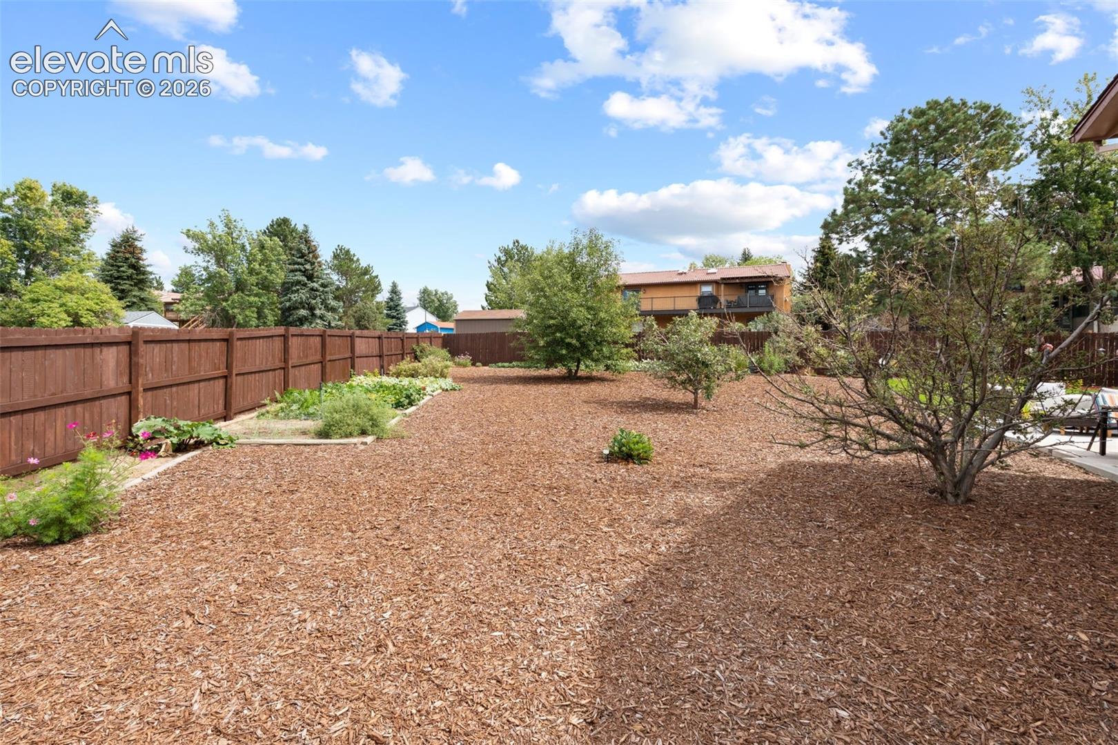 Expansive backyard featuring a wood privacy fence, organic mulch ground cover, elevated garden beds, and mature trees