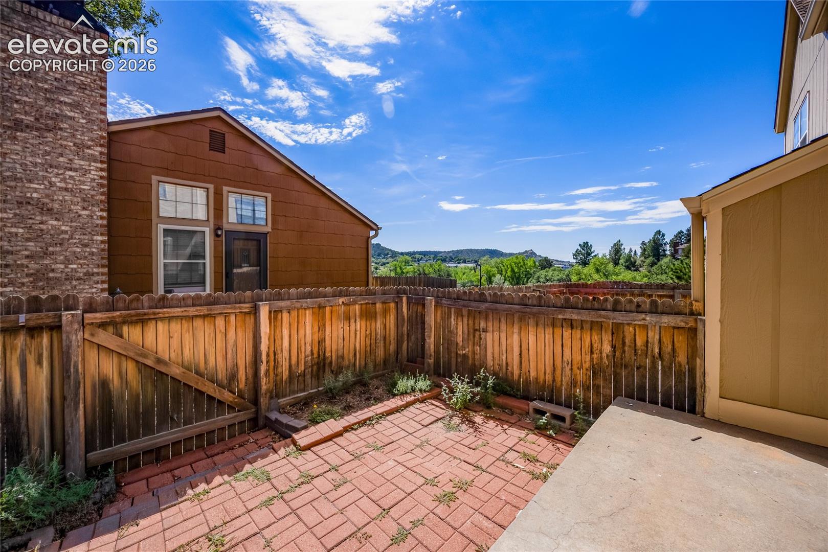 Private brick paver patio with a wood privacy fence and concrete slab area