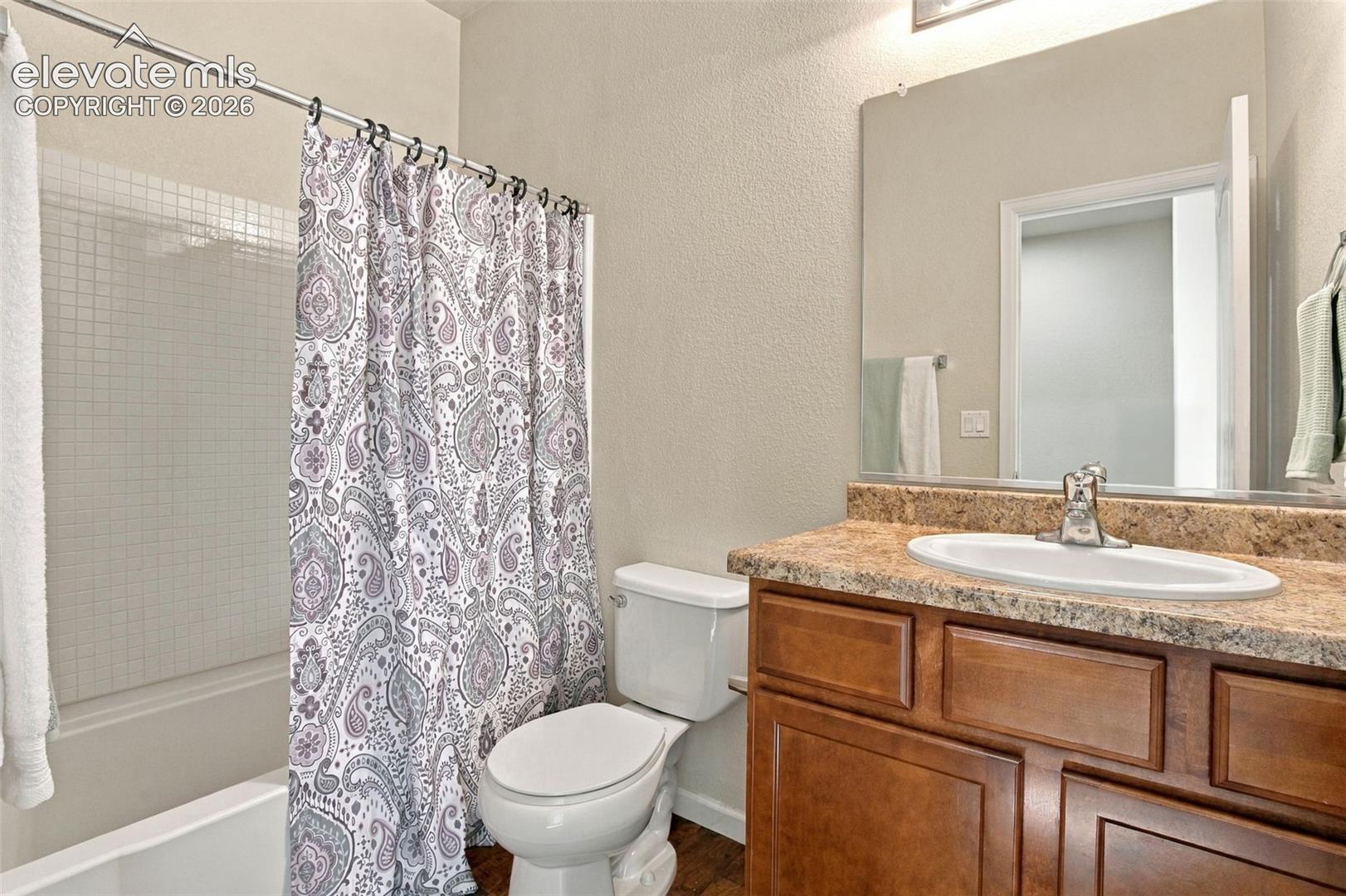 Bathroom featuring a wood-finish vanity with a stone-composite countertop, integrated oval basin, polished chrome faucet, and a large-format frameless mirror
