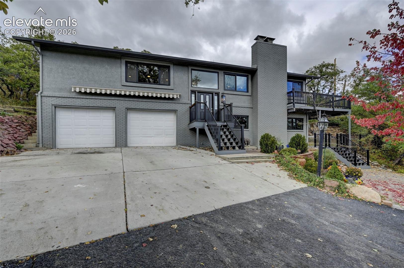 Multi-level exterior featuring a painted brick facade, integrated two-car garage, elevated deck with iron railings, and a concrete driveway