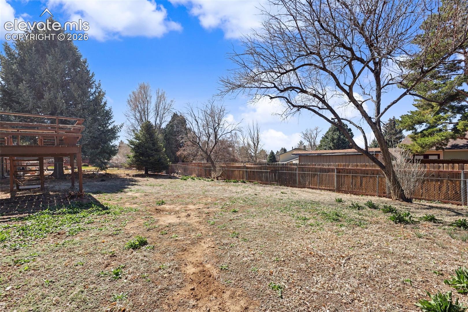 Expansive backyard featuring a tiered wooden deck, mature trees, and perimeter wood fencing